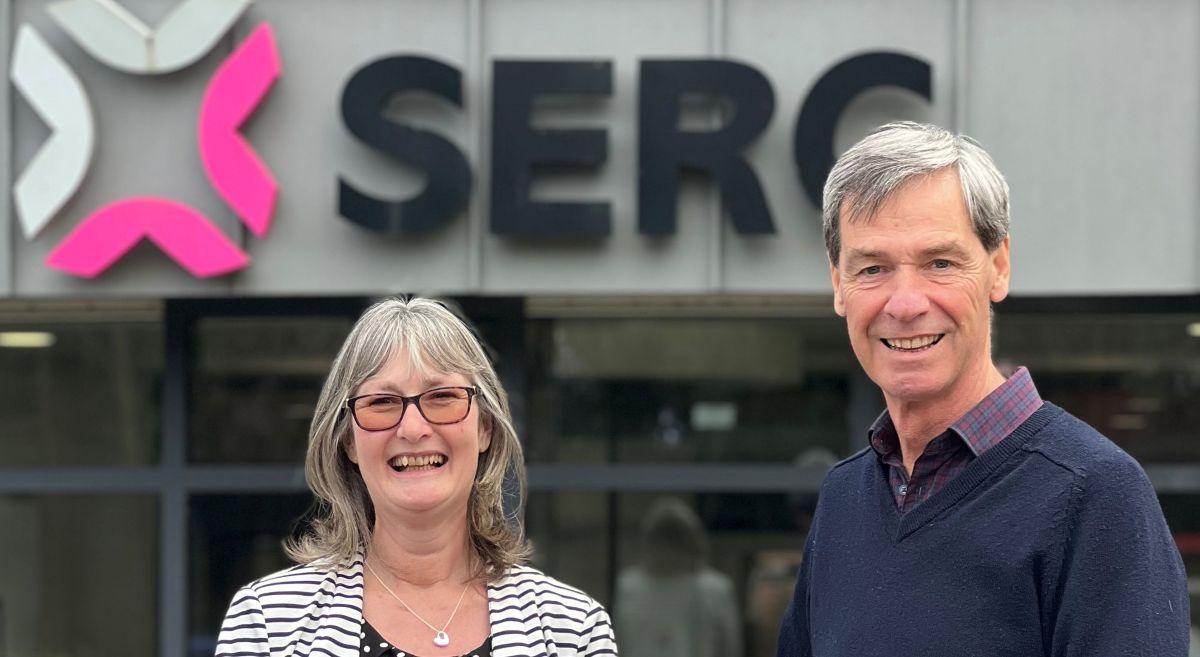 Woman and man smiling to camera with SERC logo on building in background